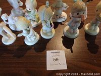 Eight small Precious Moments figurines arranged on a wooden table, showcasing various designs and pastel colors.
