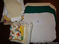 Folded stack of assorted handmade lace, crocheted doilies, assorted napkins including printed fabric and plain white napkins, with three placemats in white, cream, and green.