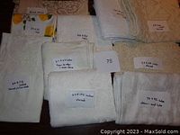 Multiple vintage white/off-white tablecloths stacked with handwritten size and condition notes visible in photo