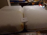 Two rectangular high density foam cushions shown side by side, light-colored with rust-colored stains on the sides.