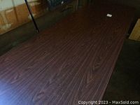 Top surface of first folding table showing dark wood grain laminate with scratches and marks.