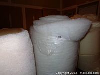 Photo showing large white roll of fiber fill batting for upholstery wrapped tightly with a label showing number 82.