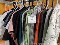 Thirteen women's clothing items hung on hangers including blouses and sweaters in a range of colors and fabrics