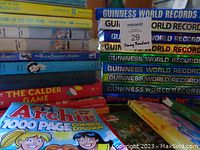 Photo shows stack of assorted young reader novels including titles such as 'The Calder Game', 'Secret of Ned Gate Farm', and others alongside several colorful Archie comics and part of the Guinness World Records books.