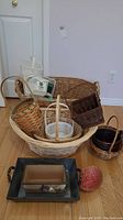 Photo showing assortment of wicker baskets including large and small sizes, white plastic basket-style containers, and decorative trays.