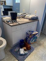 Bathroom countertop and floor showing towels, bath mat, travel bag, vases, and other bathroom items.