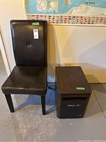 Photo of black vegan leather chair with button tufted back and four legs next to rectangular Duraflame electric heater on wheels with wood grain effect.