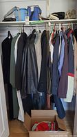 Closet rod with assorted women's clothing including jackets, blazers, coats, and some handbags on top shelf