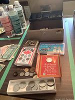 Coins and coin sets including Canadian coin sets and American commemorative sets, loose coins, and foreign money laid out next to the cash box.