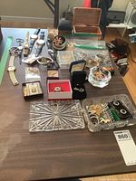 Full view of costume jewelry lot spread, showing various watches, pins, earrings, boxes and trays on table.