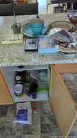Wide view of kitchen countertop and cabinet interior showing turquoise bowls, plates, spreaders, kitchen tools, and storage containers.