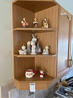 Corner kitchen shelf displaying the lot including Holt Howard Santa mug and candle hugger, Precious Moments figurines, Tengra clown, and Goebel figurines.