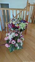 Two large faux flower bouquets arranged vertically by a wooden railing on a hardwood floor, showing overall size and presentation.