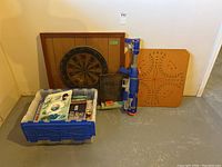 Photo of entire lot including dart board on wooden board, peg game board, Super Soaker, chalkboard, and bin of books
