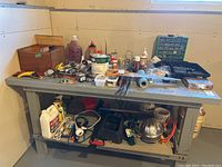 Overview of assorted hardware, tools, liquids, and other items on metal workbench with shelves below.