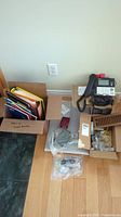 Overview photo showing box with notebooks and binders, Vtech phone base with handset, window hardware parts, vent guard, and bags of cables and other accessories.