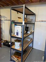 Full view of the shelving unit showing five pressboard shelves and metal frame in basement setting with items on shelves.