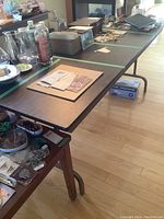 Full view of the length of the table with various items on top, showing particle board veneer surface and metal folding legs below.