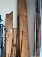 Multiple wooden scrap boards stacked upright against a garage wall, visible grain, wear and natural edges, varying widths and lengths.