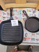 Two cast iron frying pans placed on newspaper; one round skillet and one square grill pan with ridges.