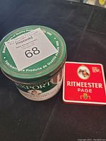 Green McDonald Export round cigarette tin and red Ritmeester Page rectangular cigarette tin on black surface.