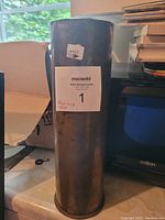 Full view of the brass WW2 shell casing standing upright showing worn patina.