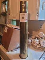 Side view of one brass WW2 shell casing standing upright showing surface and label.
