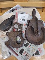 Three pulleys laid on newspaper showing rust and patina, tagged with auction label #116.