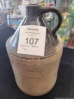 Front side of vintage ceramic jug showing brown glazed neck and handle with beige body.