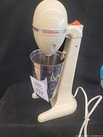 Side view of the DrinkMaster electric drink mixer set up with the stainless steel mixing cup and power cord visible.