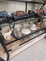 Glass display cabinet shown with various items both on top and inside, including cameras, vases, teacups, and figurines for demonstration only.