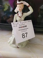 Porcelain figurine of a woman titled 'Lavina' with auction lot tag in front.