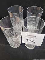Four tall glasses with etched pinwheel pattern displayed together on a black surface, clear with no visible damage.