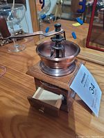 Full view of small wooden coffee grinder with metal grinding bowl, crank handle, and small drawer open below.
