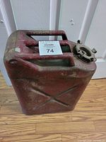 Full view of vintage red Bennett metal gas can showing its rectangular shape, two handles, embossed 'X' on the side, and screw-on cap with latch.