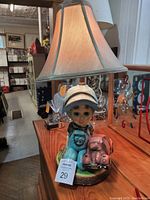 Overall front view of vintage chalkware boy lamp with toy car and shade on wooden surface