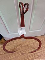 Full view of the vintage red metal ice tongs showing the large curved gripping ends and scissor-style handle on wood floor in front of white door.