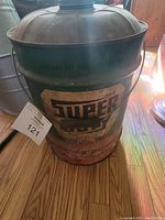 Vintage metal Super Duty oil can with original spout standing on wooden floor showing front label and rust on the surface.