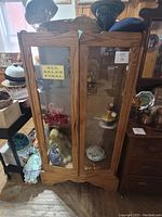Front view of the wooden glass cabinet showing two glass doors and carved wood top.