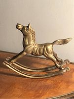 Side view of vintage brass rocking horse showing detailed mane, saddle, raised head and curved rocker legs.