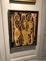 Frontal view of the framed batik artwork showing three abstract figures in black and gold tones.
