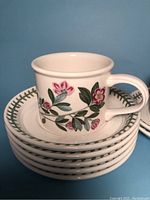 Stack of eight white ceramic cups displaying a floral design with pink and green leaves, set on matching saucers which have a green leaf pattern around the rim.
