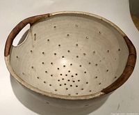 Top view of the pottery colander showing interior drainage holes and wooden rim handle.