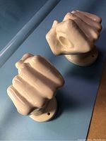 Two white ceramic hand-shaped mounts with an acrylic towel bar resting between them