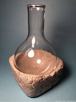 Full view of the wine carafe showing clear glass vessel inside rough-textured concrete base.