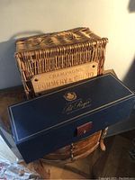 Photo of a blue Pol Roger champagne box stacked in front of a Pommery & Greno wicker basket labeled on a metal plate.