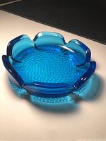 Top view of vibrant electric blue glass dish showing textured pebble pattern and scalloped flower petal edge.