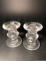 Pair of clear textured glass candlesticks designed by Staffan Gellerstat for Pukeborg, shown upright side by side on black background.