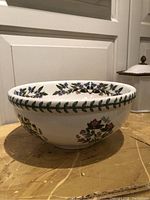 Side view of the bowl showing the white ceramic surface with flower and leaf designs on the exterior and the leaf border around the top edge.