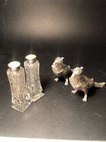 Pair of cut glass salt and pepper shakers with sterling silver tops and pair of sterling silver pheasant-shaped shakers shown together.